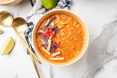 a bowl of soup with tortilla chips and limes on the side next to it