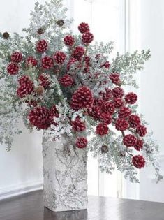 a white vase filled with red flowers on top of a wooden table next to a window