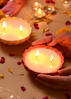 two people holding candles in their hands on a table with rose petals and petals around them