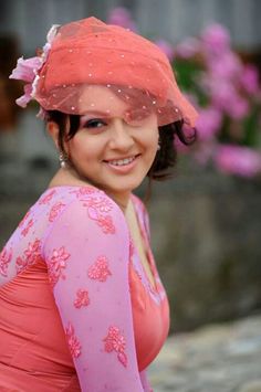 a woman wearing a pink dress and hat with flowers on it's head, posing for the camera