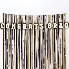 the congrats grad banner is hanging in front of a white wall with black and gold stripes