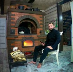 a man sitting on a chair in front of an open fire place and looking at his cell phone