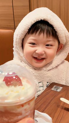 a little boy sitting at a table with a cup of ice cream in front of him