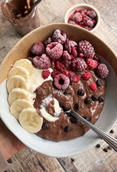 a bowl filled with chocolate pudding, bananas and raspberries on top of a wooden table