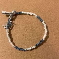 a blue and white string bracelet with tassels sits on a brown table top