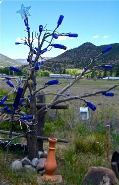 a tree with blue bottle caps stuck to it's branches in the middle of a field