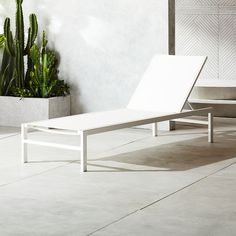 a white lounge chair sitting on top of a cement floor next to a potted plant