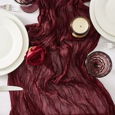 the table is set with white plates, silverware and red rose petals on it