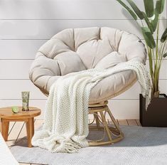 a chair with a blanket on it next to a potted plant and a table