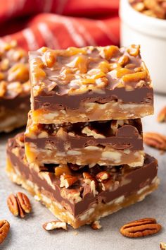 three pieces of chocolate pecan bar stacked on top of each other with pecans around them