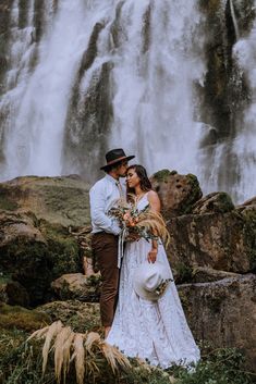 a bride and groom standing in front of a waterfall