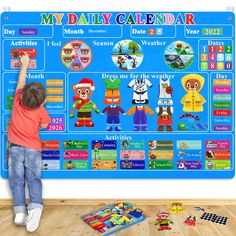 a young boy standing in front of a large calendar on a wall with stickers