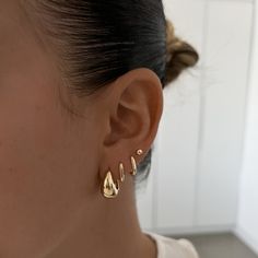 a close up of a person's ear wearing two gold earrings and a white t - shirt