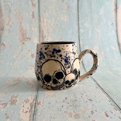 a coffee cup with skulls painted on it sitting on a wooden table next to a wall