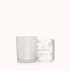 a white candle next to a box on a white surface with snow flakes all over it