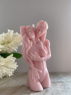 a pink ceramic figurine with two hands on it next to a white flower