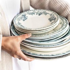 a stack of white and blue plates stacked on top of each other in front of a woman's hand