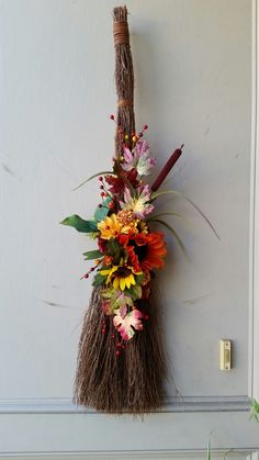 a broom hanging on the wall with flowers and leaves attached to it's side