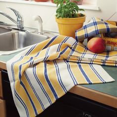 a kitchen sink with a dish towel, potted plant and fruit on the counter