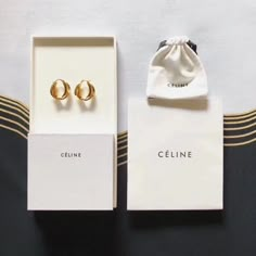 two pairs of gold earrings sitting on top of a white box next to each other