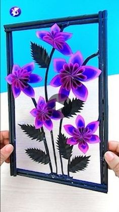 a person holding up a card with purple flowers on it and black leaves in the middle