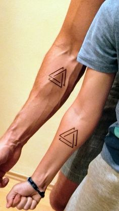 two people holding hands with tattoos on their arms and one has a small triangle in the middle