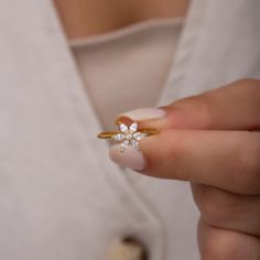 a woman's hand holding a gold ring with two small white flowers on it