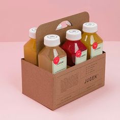 three bottles of juice in a box on a pink surface