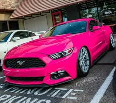 a pink mustang parked in front of a building with two other cars behind it on the street