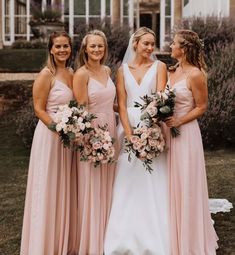 four bridesmaids standing in front of a house with their dresses pulled back and holding bouquets