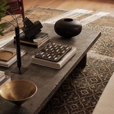 a coffee table with books and a vase on it in front of a couch next to a rug