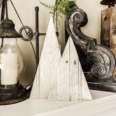 two white wooden christmas trees sitting on top of a mantle next to a candle holder