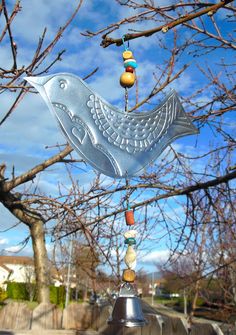 a metal bird wind chime hanging from a tree with blue sky in the background