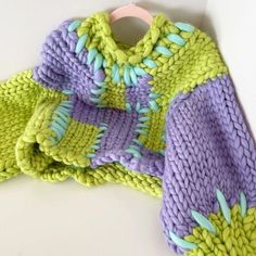 a green and purple knitted sweater sitting on top of a white table next to a wooden hanger