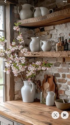 a kitchen counter topped with white vases filled with flowers next to a brick wall