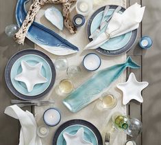 the table is set with blue and white plates, silverware, and starfish napkins