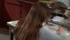 a woman writing on a piece of paper in front of a counter with other items