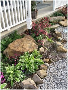 a garden with rocks and flowers next to a white porch railing on the side of a house