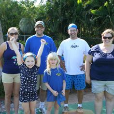 a group of people standing next to each other on a green surface with trees in the background