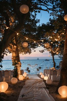 an outdoor wedding setup with paper lanterns strung from the trees and chairs on the beach