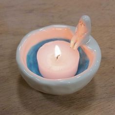 a small white candle in a bowl on a wooden table with a little figurine