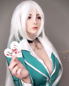 a woman with long white hair holding a heart shaped card in her right hand and looking at the camera