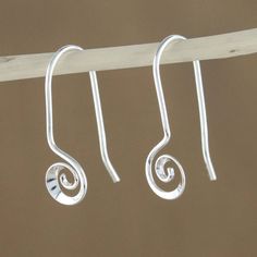 three silver spiral earrings hanging from a wooden hanger on a white string against a brown background