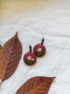 two small red and white flowers are sitting on some brown leaves