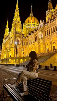 a woman sitting on top of a bench in front of a large building at night