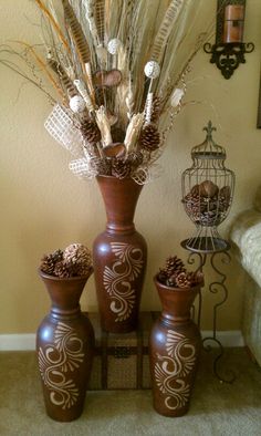 three brown vases filled with dried plants and pineconis in front of a wall