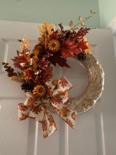 a wreath with fall leaves and flowers hanging on the front door