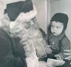 an old black and white photo of santa claus reading to a toddler who is wearing a hat