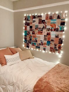 a white bed topped with lots of pillows next to a wall covered in pictures and lights