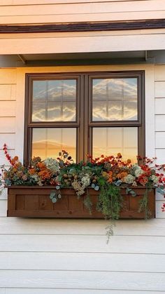 a window box filled with flowers on the side of a white building at sunset or dawn